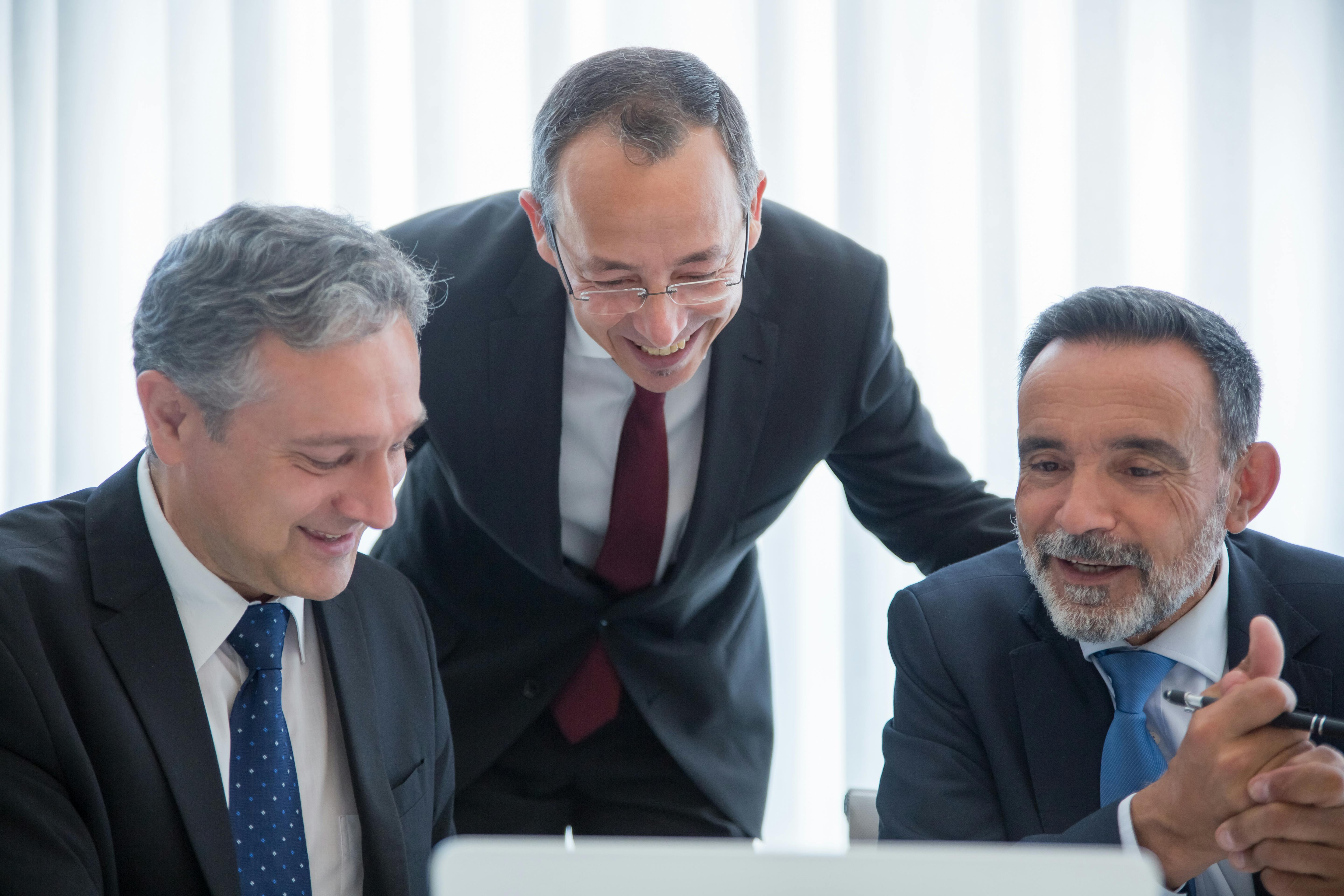 Three businessmen in suits engaging in teamwork indoors with smiles.